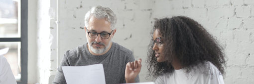 Zwei Kollegen lesen gemeinsam ein Dokument auf einem Blatt Papier